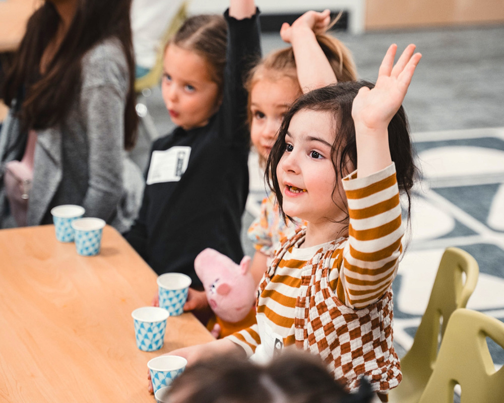 children sitting at table raising hands